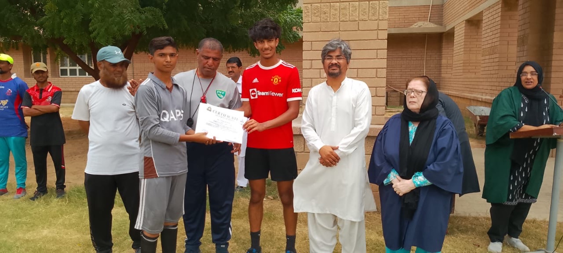 Taimur Naeem and QAPS staff hand a student a certificate after the football week.